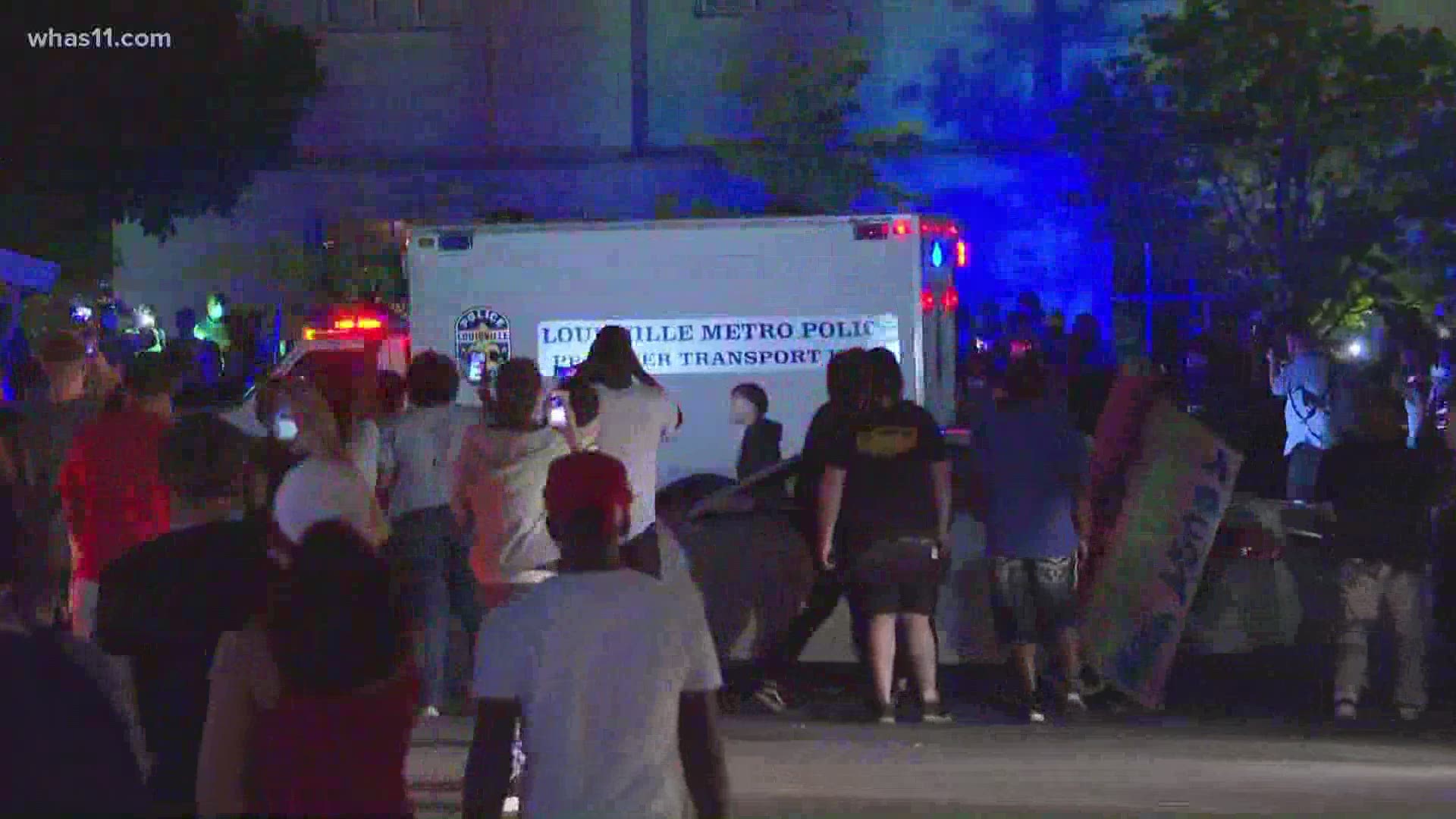 Protesters rock LMPD vehicle back and forth. Shortly after, the crowd begins to disperse when loud bangs are heard.