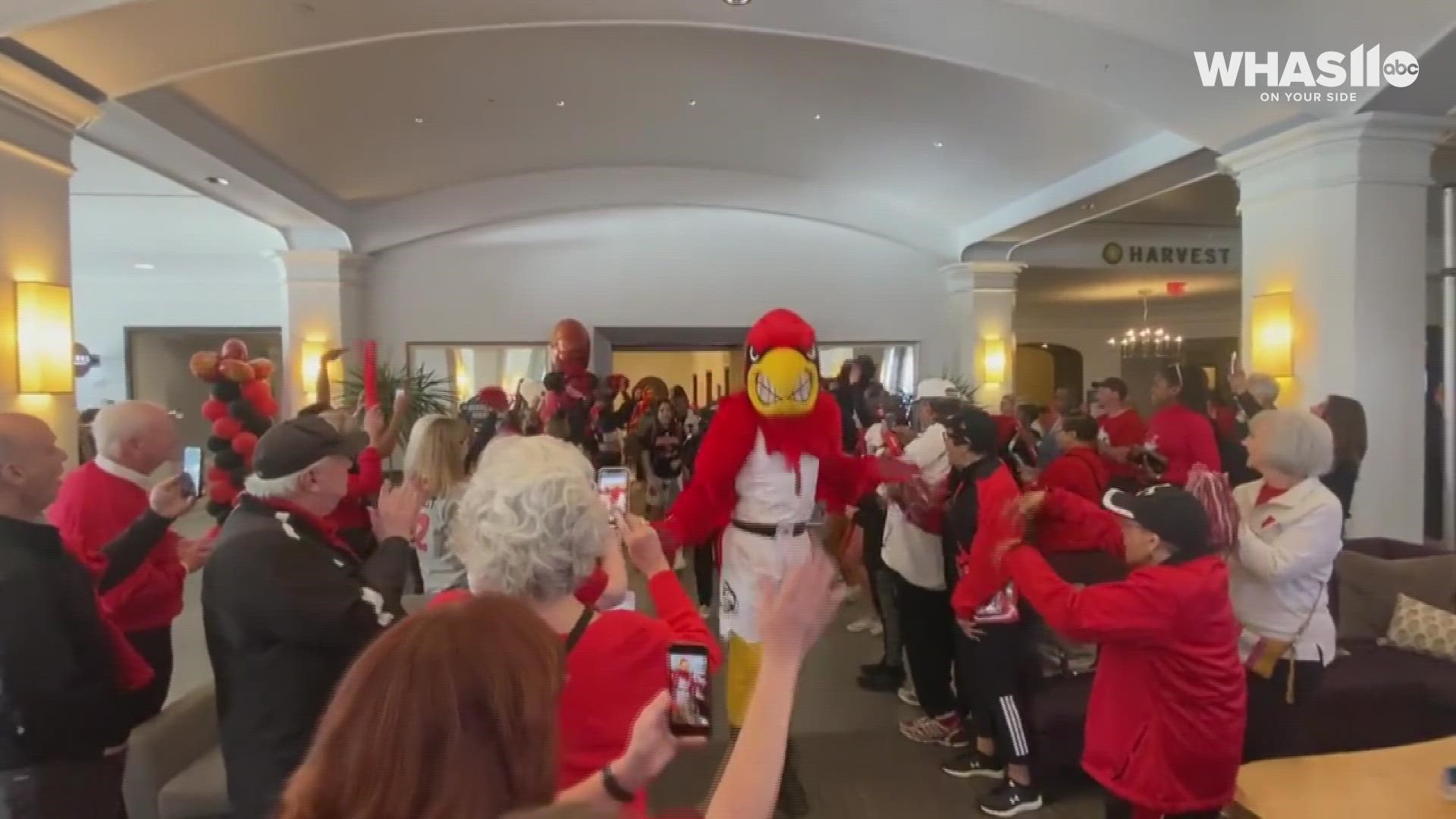 Coach Jeff Walz and members of the Louisville Cardinals basketball team receive a loud, cheerful send-off from fans before their Elite 8 match against Michigan.